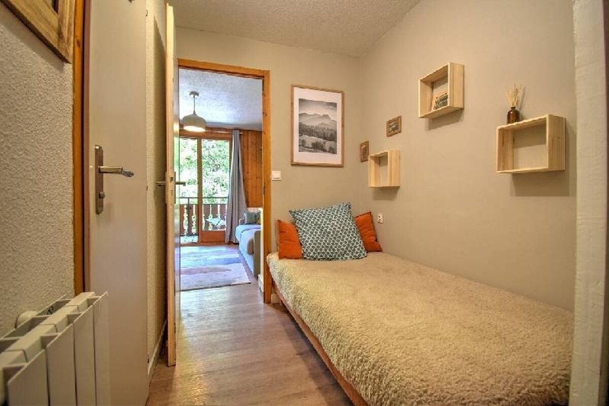 Small, cozy bedroom with a single bed, floating wooden shelves, and an open doorway leading to a balcony.