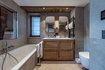 A chic, modern bathroom featuring a bathtub, wooden double vanity with a mirror, and rustic wood ceiling accents over gray tiled walls.
