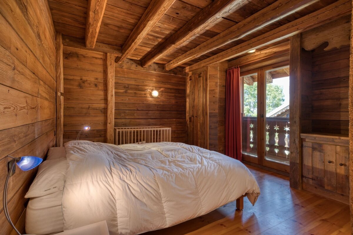 Cozy wooden cabin bedroom featuring a bed with a white duvet, a wooden crib, and glass balcony doors.