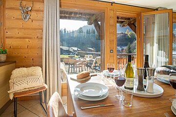 Cozy alpine cabin dining room with a set table and wine, overlooking a scenic mountain view.