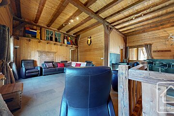 Rustic wood-paneled living room with exposed ceiling beams, leather sofas, a bar, and colorful accents. It has a cozy chalet feel.