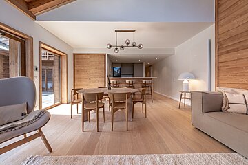 Bright, modern open-plan living, dining, and kitchen area with light wood floors and furniture, and natural light.