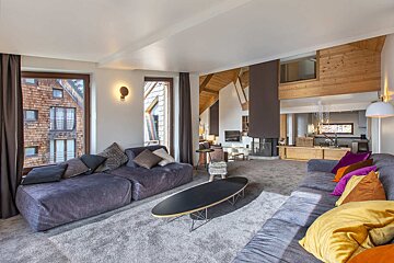 Modern chalet living room featuring large gray sectional sofas with colorful pillows, a sleek oval coffee table, and wood-paneled walls.