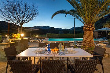 A table with a bowl of oranges on it in front of a pool