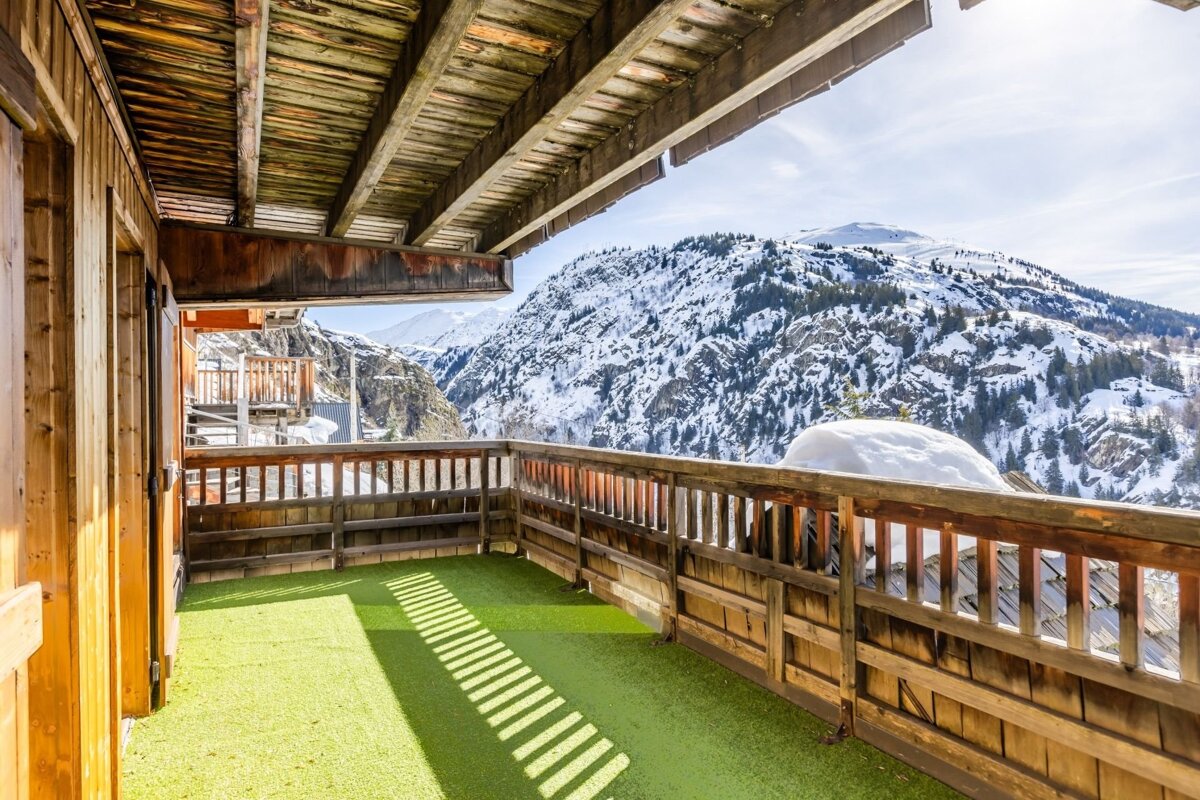 A wooden chalet balcony with green turf flooring overlooking snow-covered mountains.