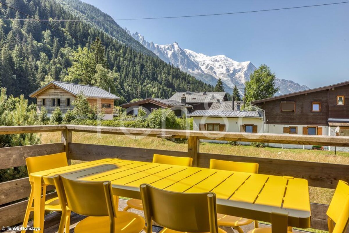 A yellow table and chairs on a balcony with mountains in the background