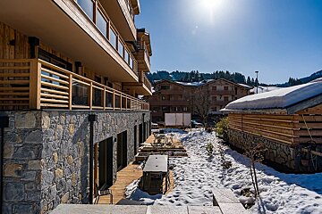 Wooden alpine chalets with stone bases next to a snow-covered patio under a bright sunny sky.