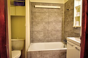A bathroom with orange tiled walls, a white bathtub, and a white sink set into a dark brown countertop, with visible pipes underneath.
