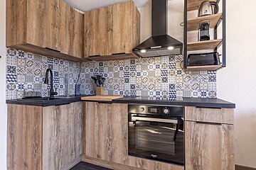Compact, modern kitchen featuring wood-grain cabinets, black countertops, a colorful geometric tile backsplash, and built-in appliances.