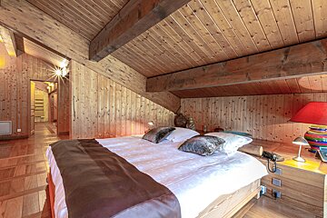 A rustic, wood-paneled attic bedroom features a double bed, sloped ceiling, and warm lighting, creating a cozy and inviting ambiance.
