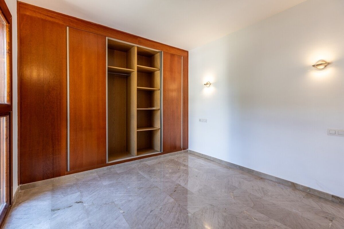 Empty room with white walls, marble flooring, and a large built-in wooden wardrobe with sliding doors, partially open to show shelves.