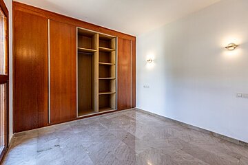 An empty room featuring a large, built-in wooden closet, marble tile floors, and plain white walls with two light fixtures.