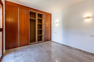 Empty room with polished marble flooring, white walls with sconces, and a large built-in wooden wardrobe with open shelves.