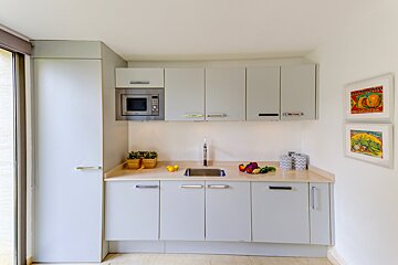 A kitchen with a sink a microwave and a picture of a pumpkin on the wall