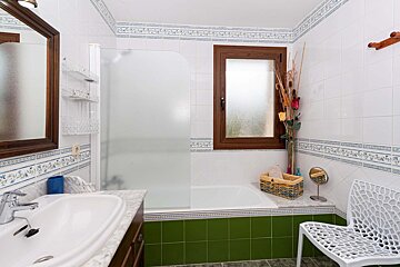 A bathroom with green tiles and a white chair