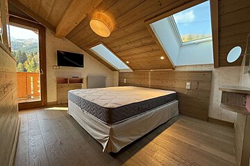 Cozy attic bedroom with wooden decor, a large bed, skylights, and a balcony offering a view of mountains and a forest.