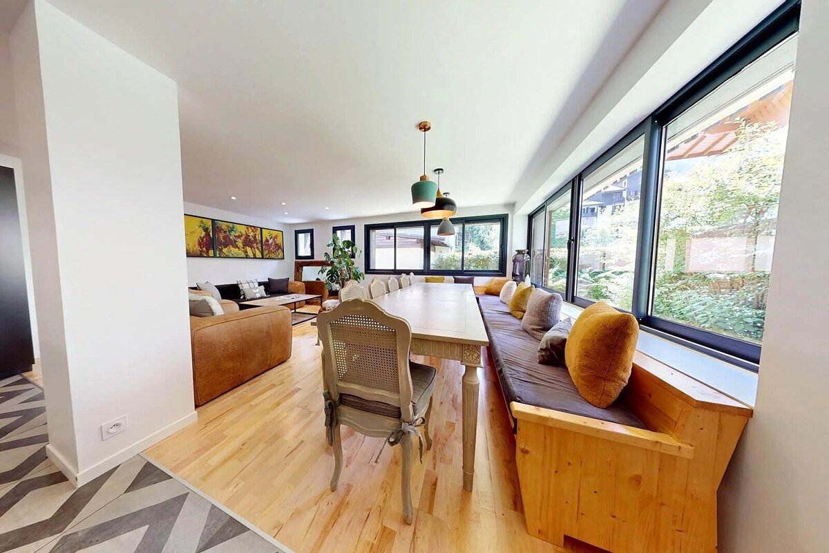 Spacious open-plan living and dining room with hardwood floors, a long table, window banquette seating, and a comfortable lounge area.