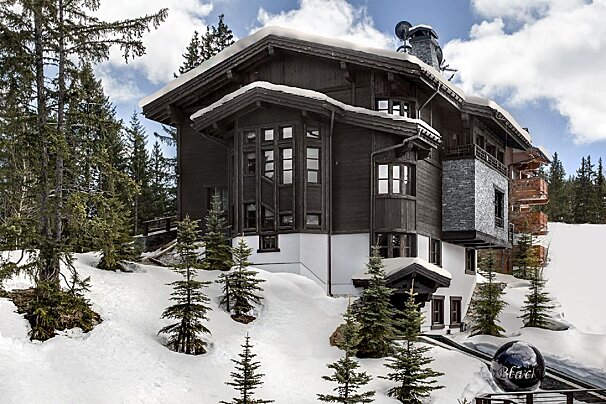 A large black and white house is surrounded by snow and trees