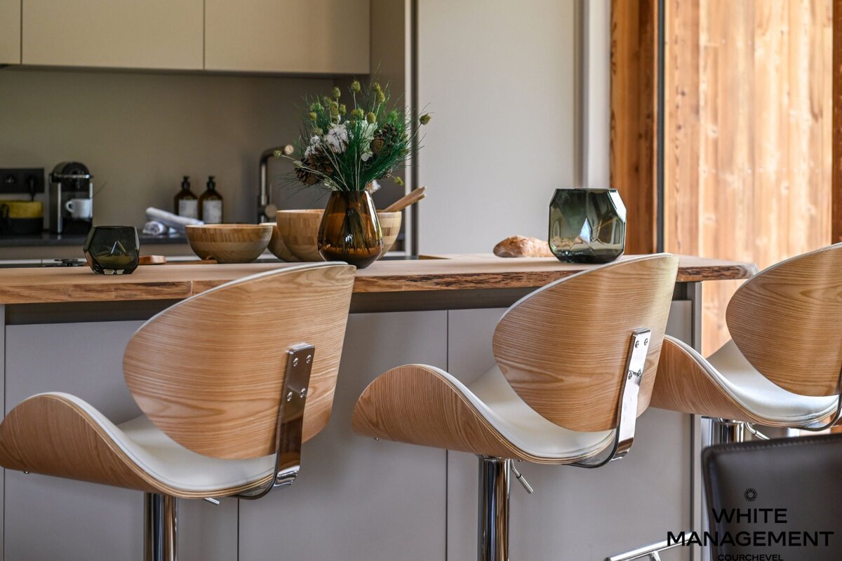 Modern kitchen island with stylish curved wooden bar stools, a live-edge countertop, and elegant decorative accents.