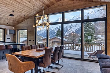 A cozy chalet dining room with large windows overlooking snowy mountains.