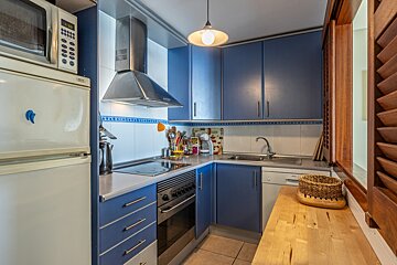 A compact blue and white kitchen with modern appliances like a fridge, microwave, and stove. Wooden shutter and countertop add a cozy feel.