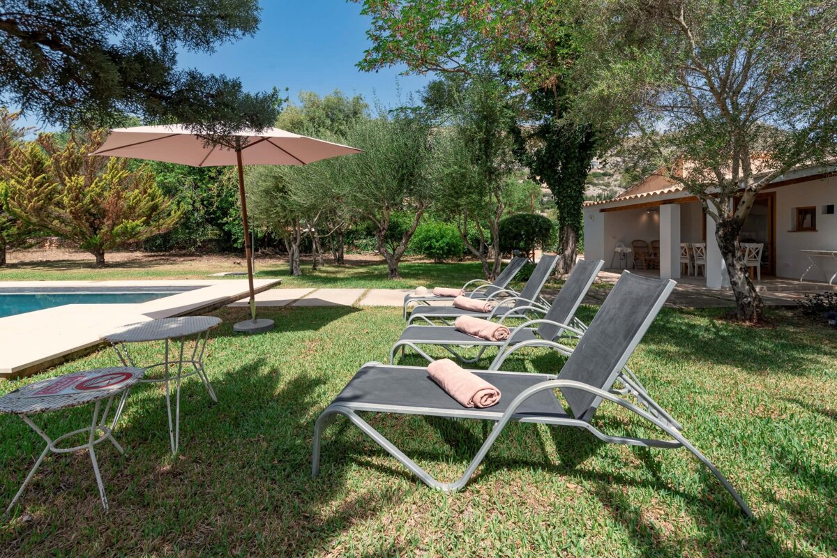 Lawn chairs with towels on them sit under an umbrella near a pool