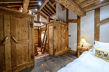 Rustic wooden bedroom with exposed beams, built-in wardrobes, and a bunk bed with a ladder, showcasing a cozy, chalet-style interior.