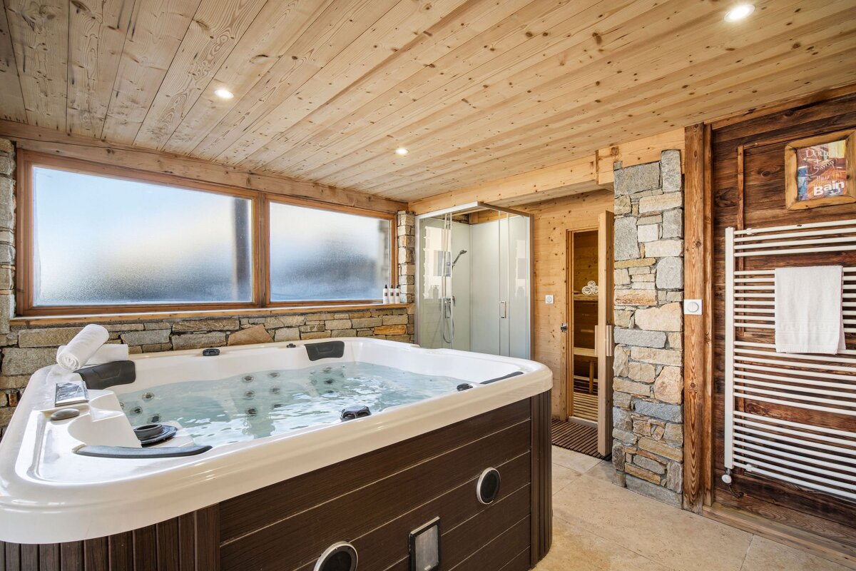 Rustic indoor spa featuring a large hot tub, wood-paneled ceiling, stone walls, a shower, and a sauna.