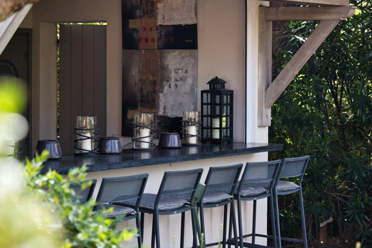 An outdoor bar with a black counter, several stools, candles in glass holders, and a large black lantern.