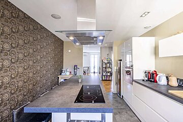 Modern kitchen with a long island stovetop, white cabinetry, and a striking patterned accent wall, leading into another room.
