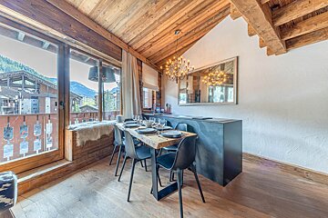 Cozy chalet dining room with rustic wooden decor, a modern table, and a large window offering stunning mountain views.