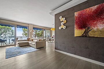 Modern living room with wood floors, a beige sectional sofa, and glass sliding doors leading to a balcony with sea views.