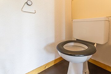 A toilet with a black seat sits in a bathroom next to a paper towel holder