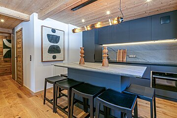 Modern kitchen with dark cabinets, light wood accents, an island with bar stools, and abstract art.
