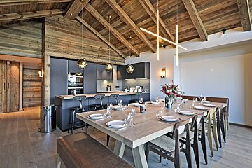 Stylish open-plan kitchen and dining room with a long table, dark cabinetry, and a striking vaulted wooden ceiling with exposed beams.