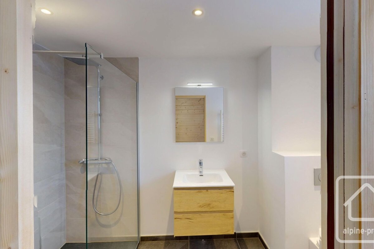 A modern bathroom with a glass-enclosed shower, a sink with a wooden vanity, a mirror, and white walls.