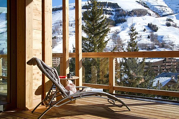 A chair sits on a deck overlooking a snowy mountain