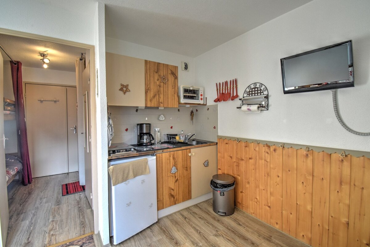 Compact kitchen with wood paneling, small appliances, a wall-mounted TV, and an open doorway to a hallway/sleeping area.