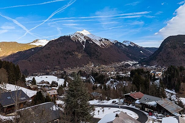A scenic alpine village nestled in a snowy valley, surrounded by towering snow-capped mountains under a bright blue sky.