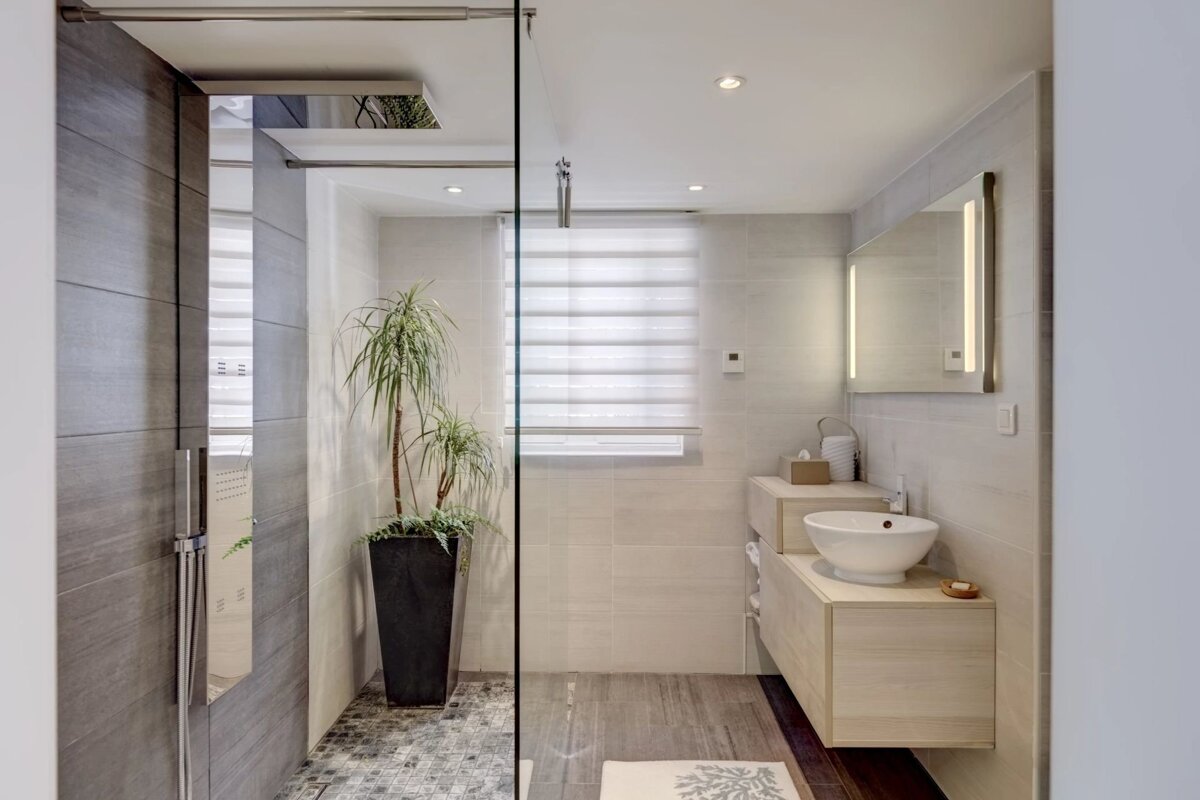 A modern bathroom featuring a walk-in shower with a large potted plant, a floating vanity with a vessel sink, and a lighted mirror.