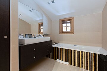 Modern bathroom with a dark wood vanity, white sink, large mirror, bathtub with vertical striped tile facade, and a small wooden window.