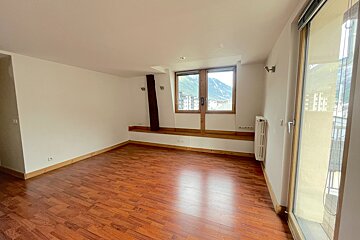 Empty room with hardwood floors, white walls, and a large window showcasing a mountain view. A balcony door is on the right.