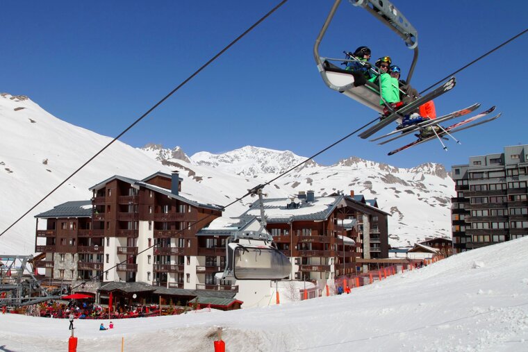 Skiers on a ski lift with a building in the background