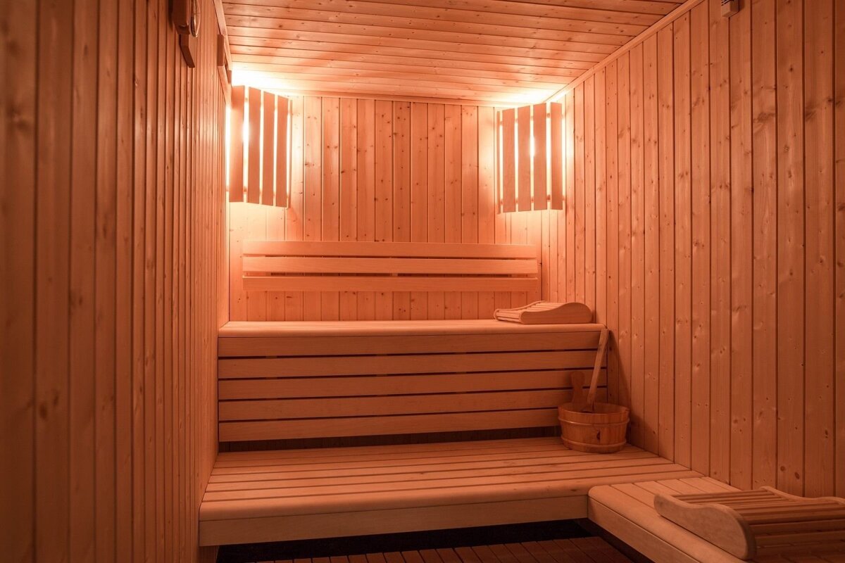 A warm, inviting wooden sauna with multi-tiered benches, soft lighting, and a traditional wooden bucket and ladle.