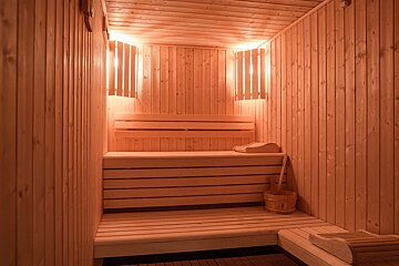 A warm, inviting wooden sauna with multi-tiered benches, soft lighting, and a traditional wooden bucket and ladle.