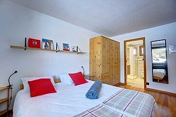 A bedroom with a bed and a shelf with books on it