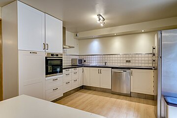 A well-lit, modern kitchen with white cabinetry, stainless steel appliances, a tiled backsplash, and light wood floors.