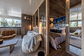 Cozy, rustic modern ski chalet interior with wood walls, stylish lighting, a separate bedroom & living area, and a panoramic mountain view.