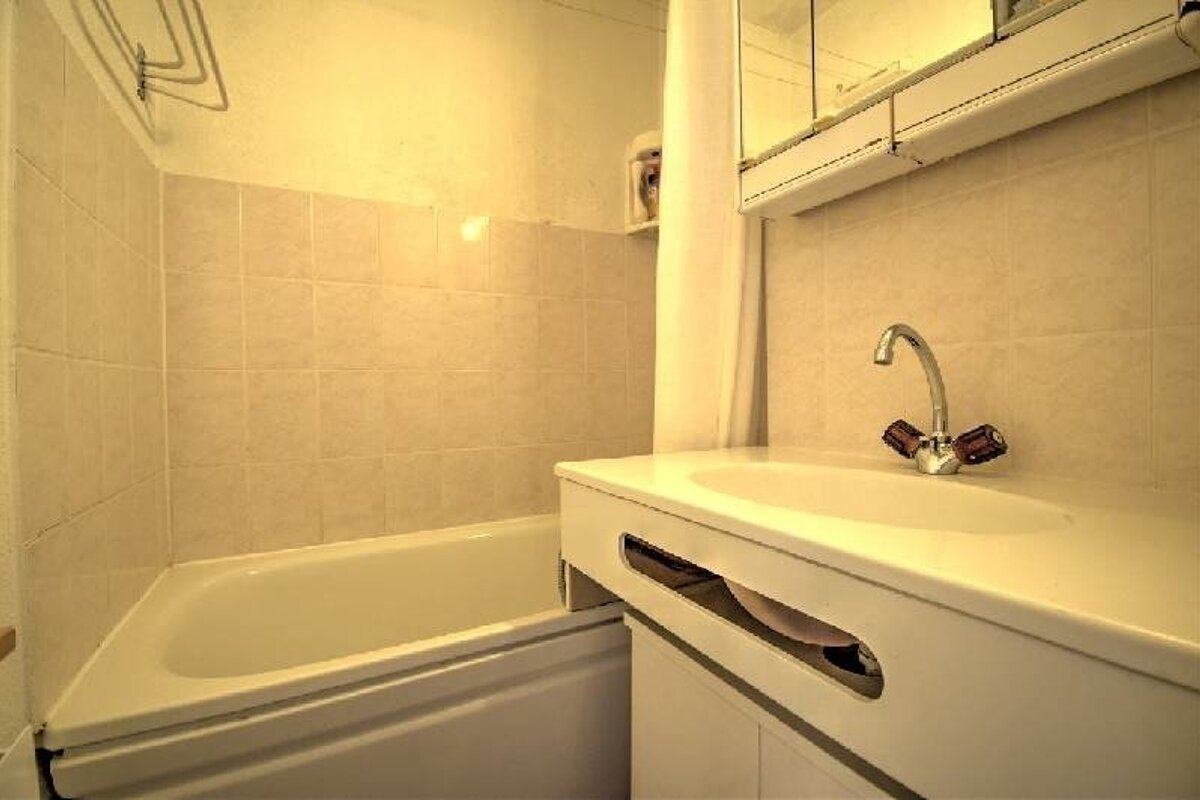 A small, warmly lit bathroom featuring a white bathtub, tiled walls, and a white vanity sink.