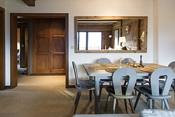 Rustic dining room featuring a grey wooden table and chairs, next to a large wood-framed mirror reflecting a cozy interior.